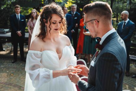 Pan Młody zakłada obrączkę Pannie Młodej podczas ślubu.