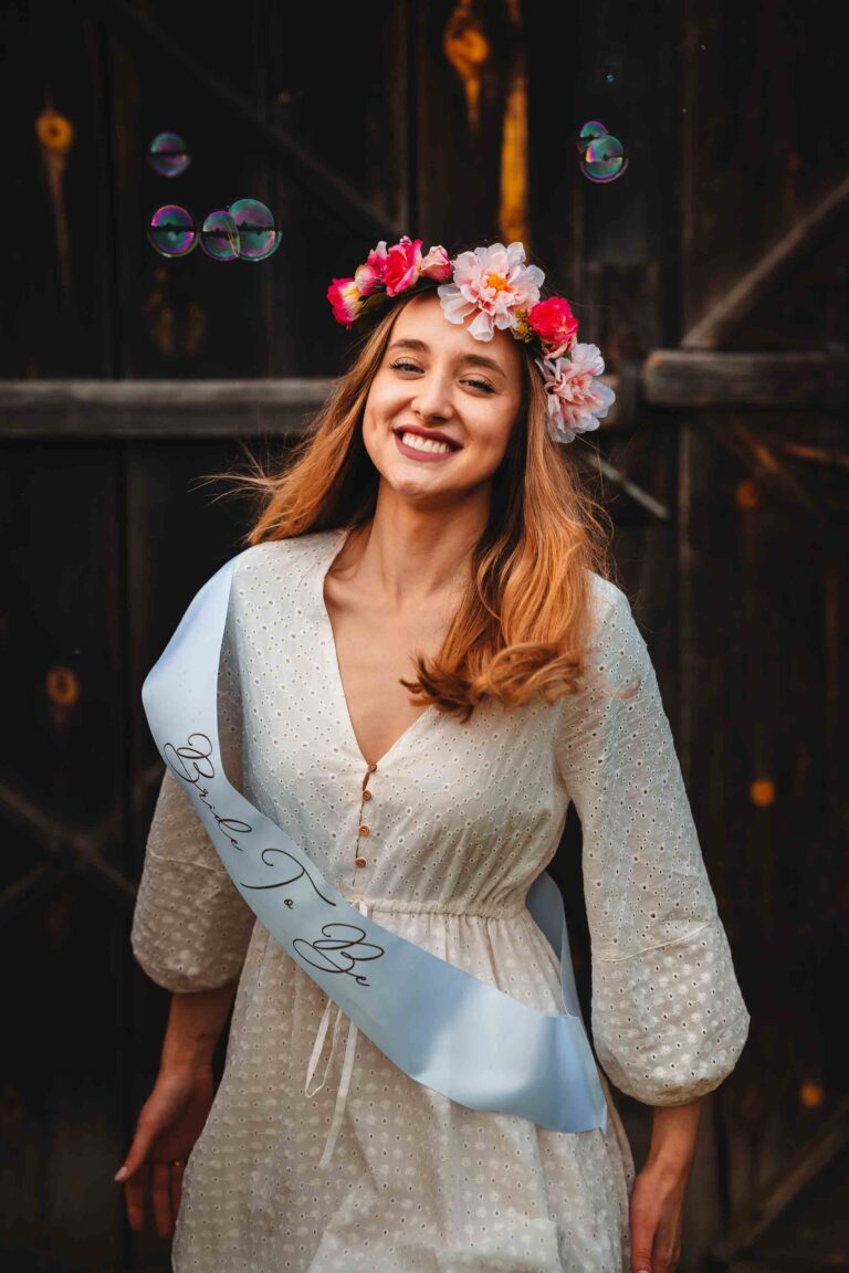 Panna młoda w wianku z kwiatów uśmiecha się na tle drewnianej ściany.