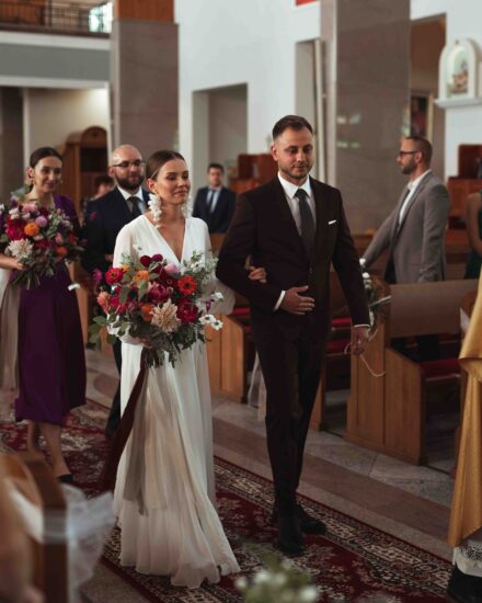 Pan Młody prowadzi Pannę Młodą przed ołtarz w kościele.