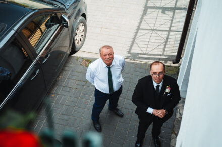 Pan Młody z ojcem spoglądają w górę w stronę fotografa ślubnego. Trwają przygotowania do ślubu.