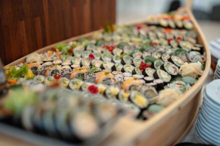 Sushi ułożone w drewnianej, miniaturowej łodzi, stoi na stole.