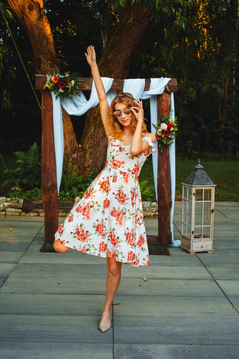 Młoda kobieta w kwiecistej sukience pozuje do zdjęcia w okularach przeciwsłonecznych