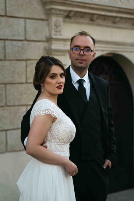 Pan Młody obejmuje Panią Młodą na tle kamienicy.