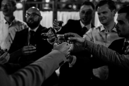 Mężczyźni wznoszą toast stukając się kieliszkami z Panem Młodym.