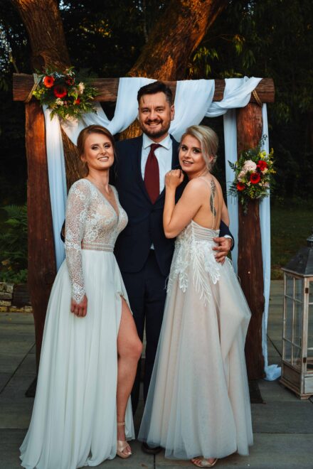 Panny Młode obejmują mężczyznę przy ślubnym kobiercu.