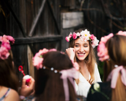 Uśmiechnięta Panna Młoda w grupie swoich druhenek na tle drewnianej ściany.