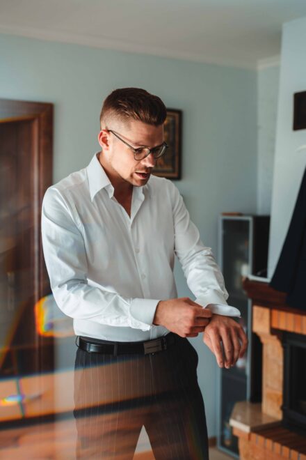 Pan Młody podczas przygotowań poprawia mankiety białej koszuli.
