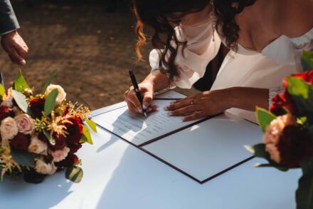 Panna Młoda podpisuje akt małżeństwa na stole z kwiatami.