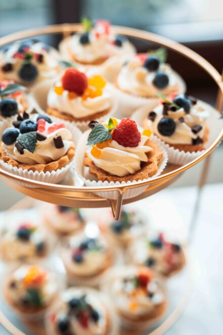 Udekorowane różnymi owocami leśnymi babeczki kremowe ułożone na dwupoziomowej tacy.