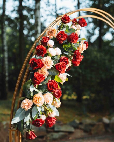 Czerwone i różowe róże upięte w ozdobne bukiety wiszą na złotym łuku.